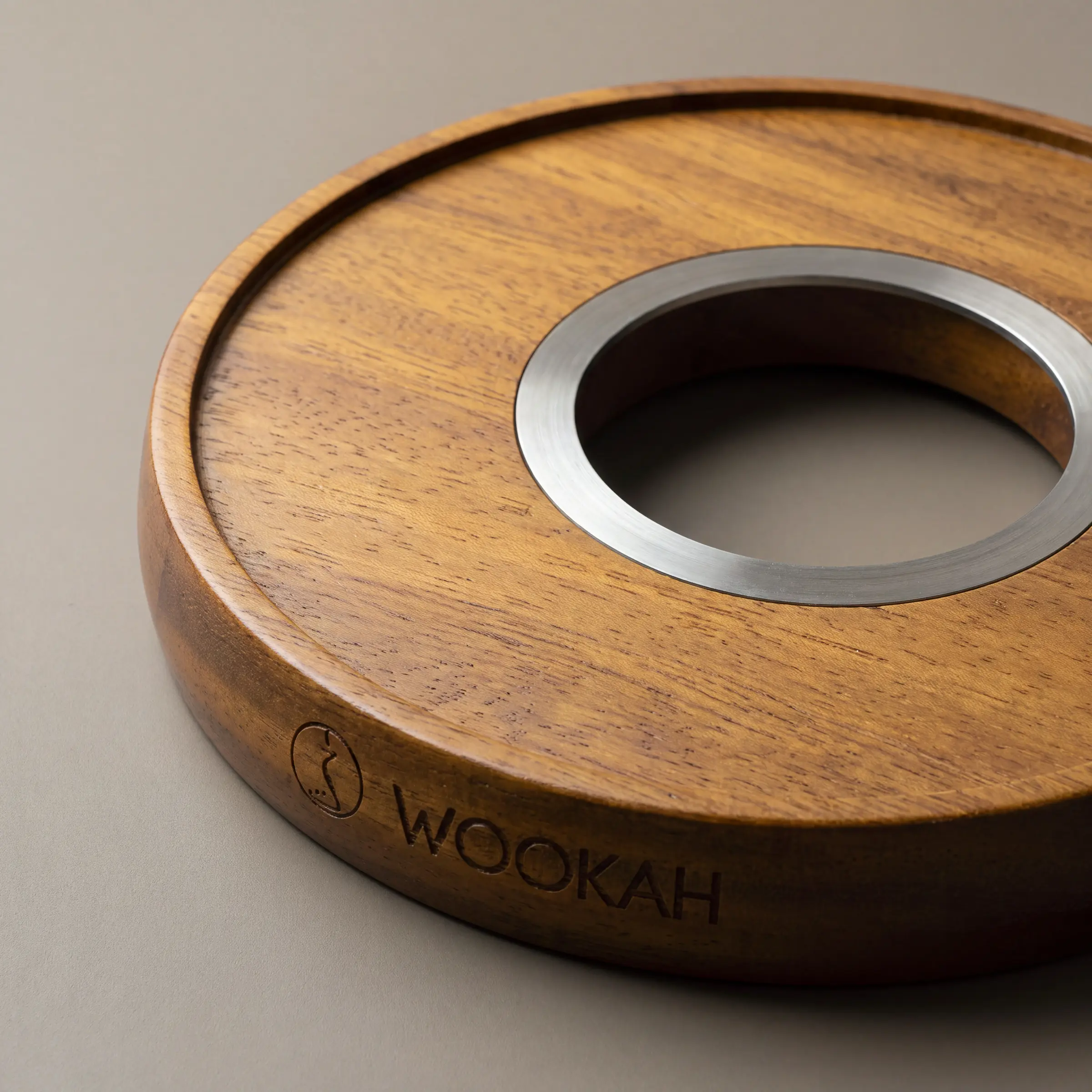 Detail: leerer Holz-Untersetzer aus Iroko mit Edelstahlring und WOOKAH-Gravur vor warmgrauem Grund