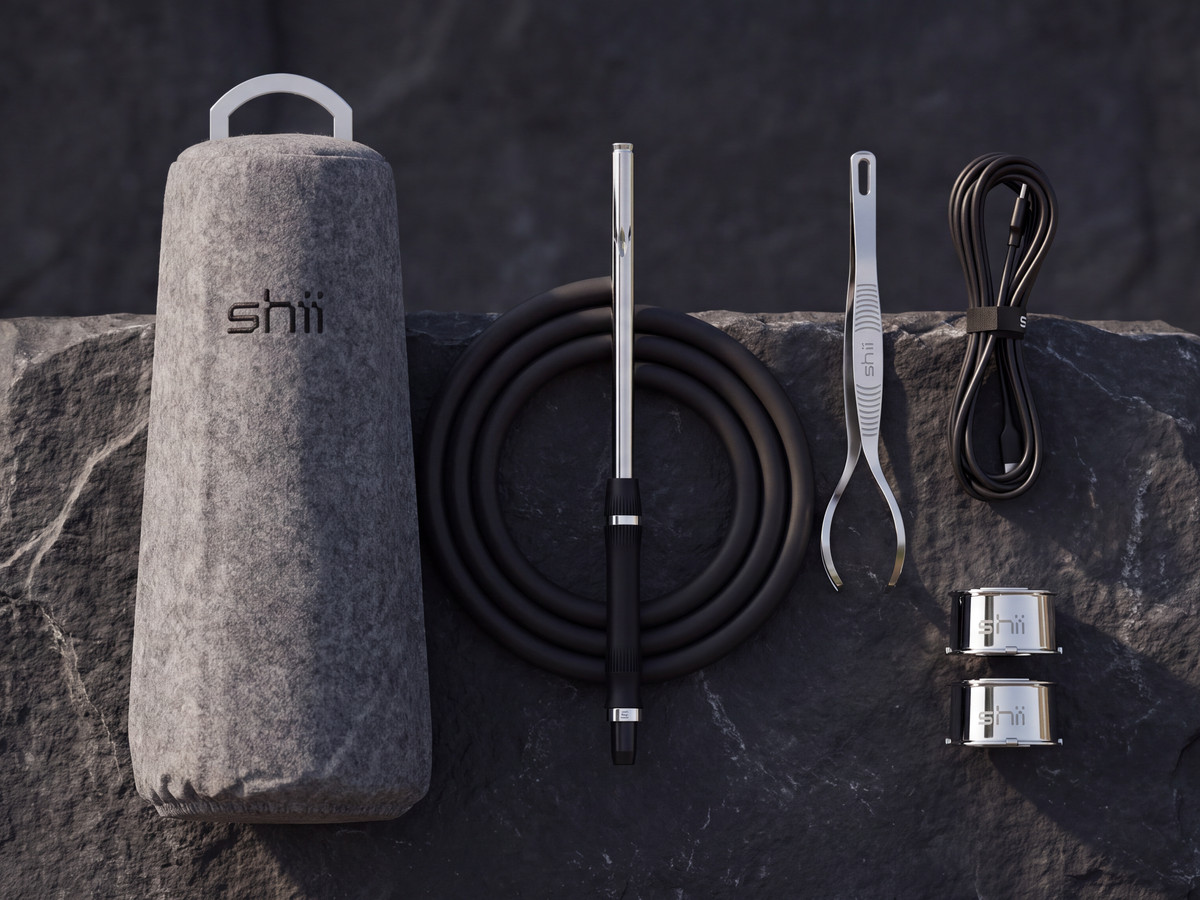 Lieferumfang der shii auf dunklem Stein: Staub-Cover, Soft-Touch-Schlauch mit Mundst&uuml;ck, Pod-Zange, USB-C-Kabel und zwei Edelstahl-Pods
